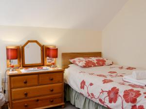 a bedroom with a bed and a dresser with a mirror at Ysgubor Uchaf - 29517 in Fairbourne