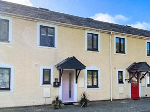 a yellow house with a red door and windows at Mill Cottage in Aberdyfi