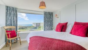 a bedroom with a large window and a bed with red pillows at Borth Mawr in Rhosneigr