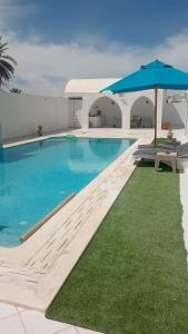 a swimming pool with an umbrella next to a building at Villa privee Narjess grande piscine et jacuzzi in Taguermess