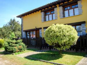 a yellow house with a black fence and a tree at APARTAMENTOS MARIAJE in Barro de Llanes