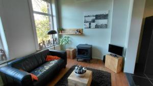a living room with a black leather couch and a stove at B&B De Gastfabriek in Tielt
