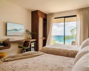 a bedroom with two beds and a desk with a window at Iguana Surf Boutique Hotel Tamarindo Rooftop Pool & Beachfront Suites in Tamarindo