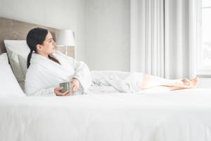 a woman in a robe laying in bed holding a mug at Maison Jenny Hotel Restaurant & Spa in Hagenthal-le-Bas +45 photos