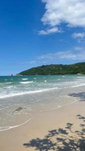 a sandy beach with the ocean and trees in the background at Pousada da Sú in Bertioga