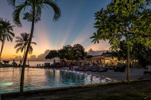a pool with palm trees and a sunset in the background at Tahiti Lagoon Resort in Punaauia