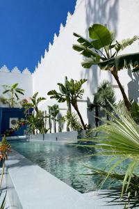 a swimming pool with palm trees in front of a building at Riad Maison de ville piscine privée in El Jadida