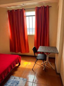 a bedroom with red curtains and a desk and a window at Pousada Popular in Três Marias