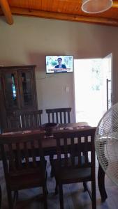 a dining room table with chairs and a tv on the wall at Cabaña LA SOÑADA in Villa Anizacate