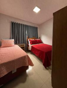 a bedroom with two beds with red sheets and a window at Casa Aconchego Lar in Rio Verde