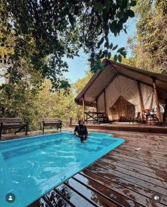 a person sitting in a swimming pool next to a tent at Bandu Buana Glamping in Kuala Pilah