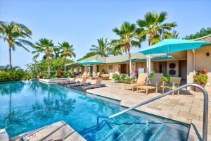 a swimming pool with chairs and umbrellas next to a house at Beautiful Ocean Villa in Kawela
