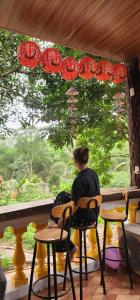 a woman sitting at a table looking out of a window at Nhà Bên Suối Retreat in Làng Tè