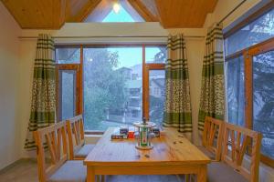 a dining room with a wooden table and a large window at Pine Wood Chalet in Manāli
