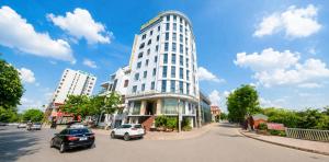 a tall white building with cars parked on the street at White Rose Hotel in Dong Hoi
