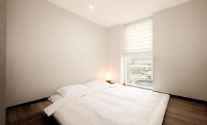 a white bedroom with a bed and a window at Venezia Hotel and Suite in Yeosu