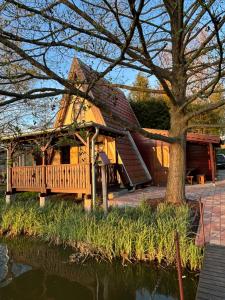 a large wooden house with a porch next to a pond at AA Apartman - Tópart in Kaposvár