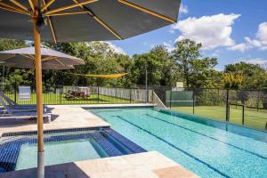 a swimming pool with an umbrella and a tennis court at Rancho Crescent Head in Crescent Head