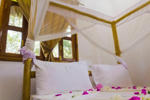a bed with white pillows and purple flowers on it at Mbao Boutique Bungalows in Jambiani