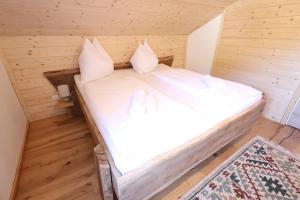 a bed in a wooden room with white sheets and pillows at Claras Bergzeit in Flattnitz
