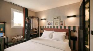 a man standing next to a bed in a bedroom at Hôtel EH OH Orly Rungis in Rungis