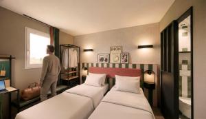 a man standing in a room with two beds at Hôtel EH OH Orly Rungis in Rungis