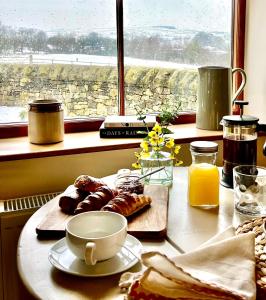 a table with a breakfast of pastries and a window at Cosy Cottage for Two in the Peak District with Parking in Onecote +4 photos