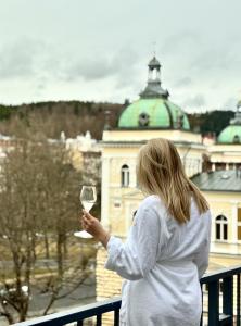 a woman holding a glass of wine on a balcony at Villa Patriot Boutique Hotel in Mariánské Lázně +68 photos