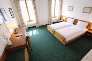 a bedroom with a bed and a desk and windows at Hotel guter Hirte in Huttwil +3 photos