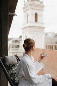 a woman sitting on a bench holding a cup of coffee at Emerald Hotel by Continental Group in Budapest