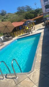 a blue swimming pool with chairs and umbrellas at Pousada Thetis in Arraial do Cabo