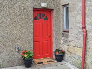 a red door on a building with two potted plants at The End Hoose in Duns