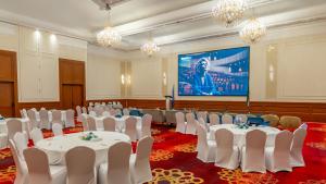 a conference room with white tables and chairs and a screen at Mövenpick Hotel & Resort Al Bida'a in Kuwait +244 photos
