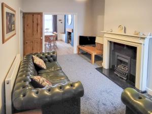 a living room with a leather couch and a fireplace at Lazy Cottage in Haverigg