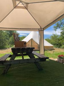 a picnic table under an umbrella with a bench and a tent at The Apple Farm Glamping in Snitterfield