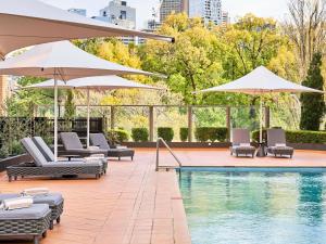 a swimming pool with umbrellas and chairs and a pool at Pullman East Melbourne in Melbourne