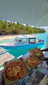 three pizzas sitting on a table next to a boat at Daisy Cottage Dhangethi in Dhangethi