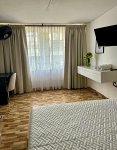 a room with a bed and a television and a table at Hotel Alamos del Bosque in Pereira