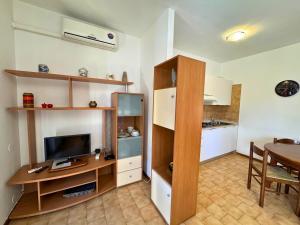 a living room with a desk with a television and a kitchen at Condominio Piscina in Grado