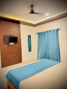 a bedroom with a bed with blue curtains and a tv at Coastal Home in Diveagar