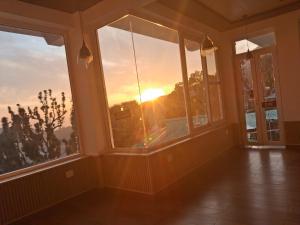 a room with windows with the sunset in the background at Nanda niwas 2 in McLeod Ganj