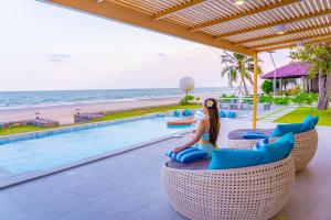 a woman sitting on a chair by the pool at a resort at Pailay Beachfront Villa Cha-Am in Ban Bang Ket