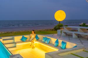a woman sitting on a bench next to the ocean at Pailay Beachfront Villa Cha-Am in Ban Bang Ket
