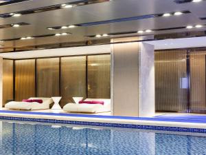 a swimming pool with two beds next to a poolasteryasteryasteryasteryasteryastery at Novotel Daqing Haofang in Daqing