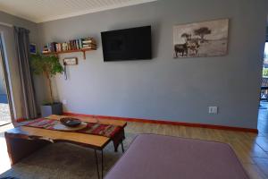a living room with a table and a tv on a wall at PINE COTTAGE Self catering fully equipped 2 bedroom, Queen bed 3 singles 65sqm cosy private cottage in Durban +16 photos