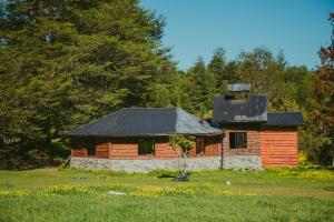a log cabin with a black roof in a field at Cabañas Shangrila Aysen in Puerto Aisén