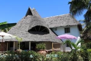 uma casa com telhado de palha e guarda-chuva em Villa Madinina em Diani Beach