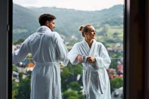 a man and a woman in white robes looking out a window at Hotel Pieniny Grand Wellness & SPA - Destigo Hotels in Szczawnica