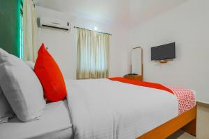 a bedroom with a bed with orange pillows and a tv at Hotel O The Goan Courtyard in Goa
