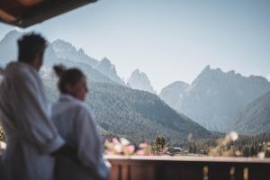Zwei Personen stehen auf einem Balkon und schauen auf die Berge. in der Unterkunft Hotel Alpenblick in Sexten